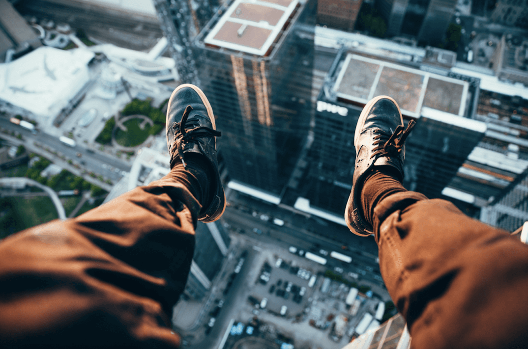 man with feet dangling from high rise building