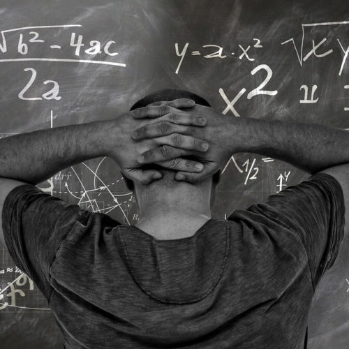 man in front of chalkboard staring at math problem