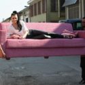 two men carrying a woman on a couch