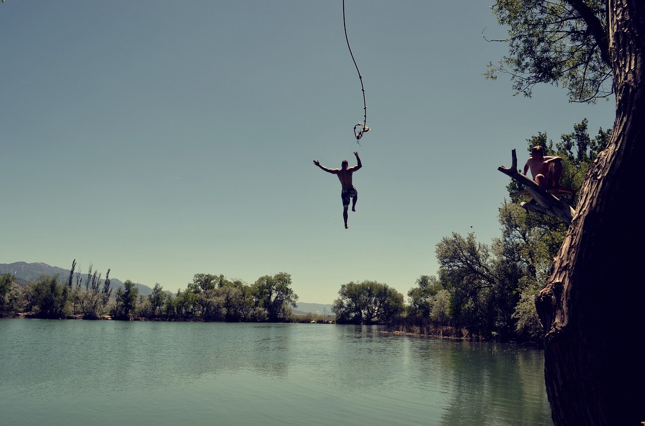 man jumping off roap into a river